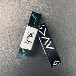 May include: Two black wristbands with white designs. One wristband has a white label with the text "EWOPT" and a stylized animal logo. The other wristband has a repeating pattern of white triangles.