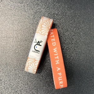 May include: Two wristbands, one with a white floral pattern and the text "Created with a purpose" in white on a coral background, and the other with a white floral pattern and the text "EWOPT" in white on a blue background.