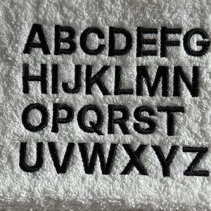 以下が含まれることがあります： 白いタオルに黒で刺繍されたアルファベットの文字AからZまで