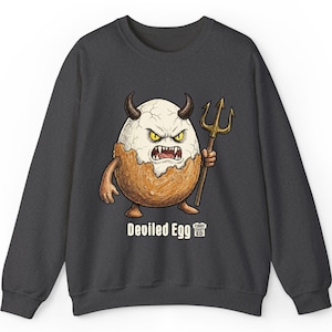 Könnte beinhalten: Dunkelgraues Sweatshirt mit einem Cartoon-Teufelsei-Charakter mit Hörnern, einem wütenden Gesicht und einem Dreizack. Der Text "Deviled Egg" steht darunter. Das Design ist in Weiß, Braun und Gelb gehalten.