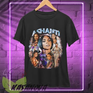 May include: Black t-shirt with a graphic print of Ashanti and other women. The text "ASHANTI" is printed in white letters on the shirt.