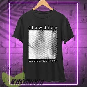 May include: Black t-shirt featuring the band name "slowdive" in white above a grayscale image. The text "souvlaki tour 1994" is below the image. The t-shirt is displayed on a wooden hanger.