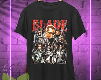 May include: Black t-shirt featuring a vintage-style graphic of the character Blade from the film Blade. The graphic depicts Blade and other characters from the film, including a motorcycle.