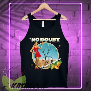 May include: Black tank top featuring the band name "NO DOUBT" in white text. The shirt has a circular graphic with a woman in a red dress, a tree, and the words "Tragic Kingdom". The tank top is hanging on a wooden hanger.