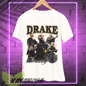 May include: Cream-colored t-shirt featuring a graphic of Drake with the word "DRAKE" in a vintage font. The design includes multiple images of Drake and the word "Drizzy" in a script font.