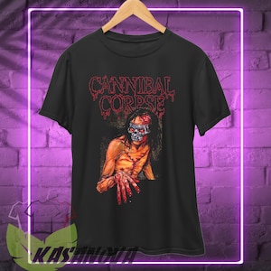 May include: Black t-shirt featuring the band name "CANNIBAL CORPSE" in red dripping letters above a gruesome illustration of a zombie with a skull face and bloody hands. The shirt is hanging on a wooden hanger.