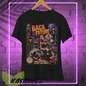May include: A black short-sleeve t-shirt featuring a Back to the Future movie graphic. The print includes the film title, characters, the DeLorean car, a clock tower, and the text: A film by Robert Zemeckis, 1985 released, and Where we're going, we don't need roads.