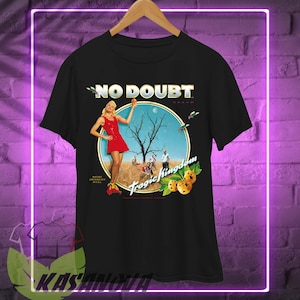 May include: Black t-shirt featuring the words "NO DOUBT" in gold lettering above a circular graphic. The graphic includes a woman in a red dress, a tree, and the words "Tragic Kingdom".