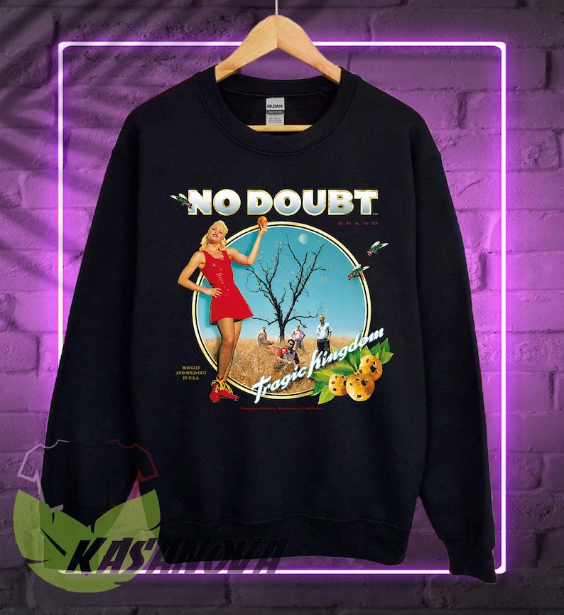 May include: Black sweatshirt featuring a graphic from the band No Doubt's album, Tragic Kingdom. The design includes a woman in a red dress, a tree, and the album title. The sweatshirt is hanging on a wooden hanger.