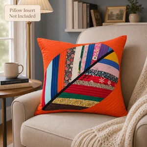 May include: A square throw pillow cover featuring a vibrant orange quilted fabric background. A large, central heart-shaped design is composed of vertical fabric strips in various colors and floral patterns. Text reads: Pillow Insert Not Included.
