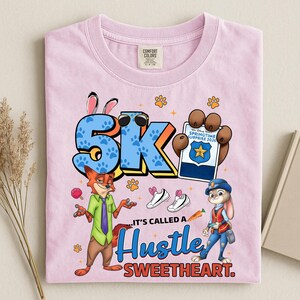 Puede incluir: Camiseta rosa claro Comfort Colors con personajes de dibujos animados y el texto "5K" con gafas de sol, huellas de patas y la frase "It's called a Hustle Sweetheart." El dise&ntilde;o incluye un zorro, un conejo y zapatillas.
