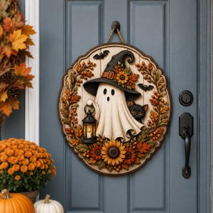 May include: A round wooden wall hanging featuring a white ghost wearing a black witch hat, holding a lantern, and accompanied by a black cat. The design is framed by autumn leaves, orange berries, and sunflowers, with two small black bats above.