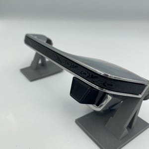 Op de afbeelding: Een zwart en zilver decoratief object met sierlijke bloemendetails. Het object wordt gepresenteerd op een grijze standaard, die het ontwerp en vakmanschap laat zien. Het item heeft een strakke, moderne uitstraling.