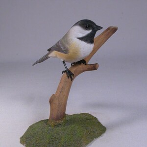 Puede incluir: Figurita de madera tallada a mano de un carbonero común posado en una rama. El pájaro está pintado con detalles realistas con plumas negras, blancas y grises. La rama es marrón y la base es verde.