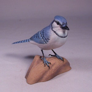 Puede incluir: Figurita de pájaro carpintero azul tallada a mano en madera, con cuerpo pintado de azul y blanco, posada sobre una base de madera marrón.