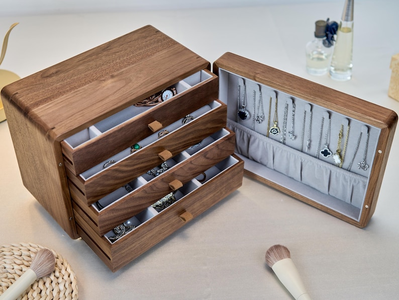 May include: A dark brown wooden jewelry box with four pull-out drawers and a hinged side compartment. The interior is lined with light gray fabric, featuring multiple small storage sections in the drawers and vertical hooks for hanging necklaces.