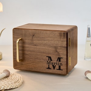 May include: A rectangular wooden storage box with a dark brown wood grain finish, featuring a gold-toned metal handle on the front, gold hinges on the side, and the engraved text "Martin" centered above a large letter "M" on the front panel.