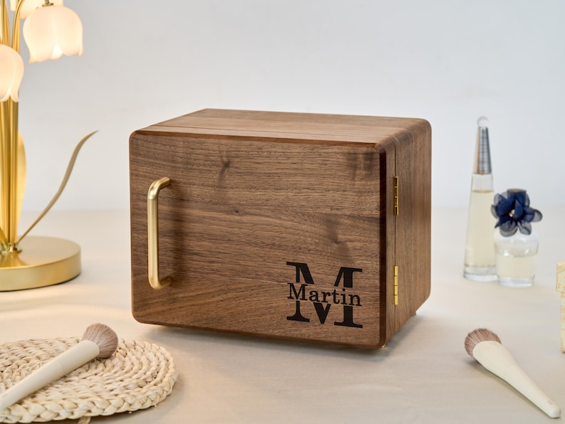 May include: A rectangular wooden storage box with a dark brown wood grain finish, featuring a gold-toned metal handle on the front, gold hinges on the side, and the engraved text "Martin" centered above a large letter "M" on the front panel.