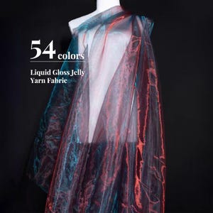 Puede incluir: Una tela transparente e iridiscente drapeada sobre un maniquí, con una paleta de colores cambiantes de azul verdoso profundo y naranja rojizo. El texto 54 colors Liquid Gloss Jelly Yarn Fabric está impreso en blanco a la izquierda sobre fondo negro.