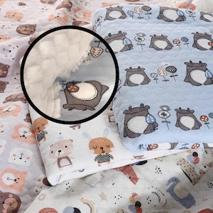 Pode incluir: Um cobertor de bebê com fundo azul claro e um padrão de animais de desenho animado, incluindo ursos e coelhos. O cobertor tem uma textura macia e acolchoada e uma borda branca e fofa. O cobertor está dobrado.