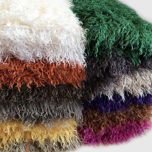 May include: A stack of folded faux fur fabric pieces in various colors including white, orange, dark gray, yellow, green, purple, and magenta. Each piece features a long, curly, shaggy texture that creates a dense and voluminous appearance.