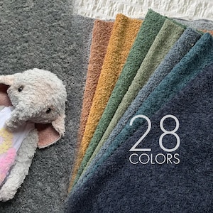 May include: A plush elephant toy with a white and pink patterned chest next to a fan of fabric swatches in various colors including tan, mustard yellow, sage green, olive, teal, and dark charcoal gray with the text 28 COLORS overlaid.