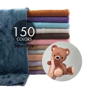 Può includere: Una pila di tessuto in finta pelliccia piegato in vari colori con un pelo di 5 mm, con un grande pezzo blu in primo piano. Il testo sull'immagine recita 150 COLORS e 5mm Pile. Un piccolo orsacchiotto di peluche marrone è in un riquadro circolare.