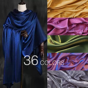 Puede incluir: Un chal azul real drapeado sobre un maniquí. A la derecha, muestras de tela en oro, rosa, verde, azul y gris. El texto dice "36 COLORES". Las telas tienen un aspecto brillante y sedoso.