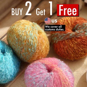 May include: Close-up of colourful yarn balls in shades of orange, blue, and pink. The yarn has a textured, fluffy appearance. Text in the image reads "BUY 2 Get 1 Free" and "US".