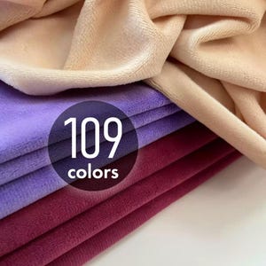May include: Stacked layers of soft, plush fabric in shades of beige, lavender, and deep burgundy. A circular black graphic overlay is centered on the fabric, featuring the white text 109 colors. The material has a visible, velvety texture.