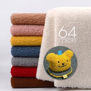Könnte beinhalten: Ein Stapel gefalteter Sherpa-Fleece-Stoff in verschiedenen Farben wie Braun, Rosa, Gelb, Blau, Grau, Rot und Dunkelbraun, mit einem großen weißen Stück mit dem Text 64 COLORS und einem runden Einsatz, der einen gelben bärenförmigen Artikel zeigt.