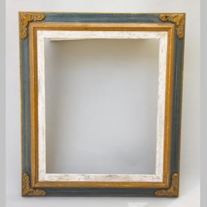 Peut inclure: Un cadre rectangulaire composé d'une bordure extérieure bleu foncé, d'une section centrale dorée et d'une bordure intérieure blanche à la finition vieillie. Les quatre coins sont ornés de volutes décoratives de couleur dorée.