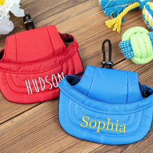 May include: Two personalized dog hats, one red with the name "HUDSON" embroidered in white and one blue with the name "Sophia" embroidered in yellow.