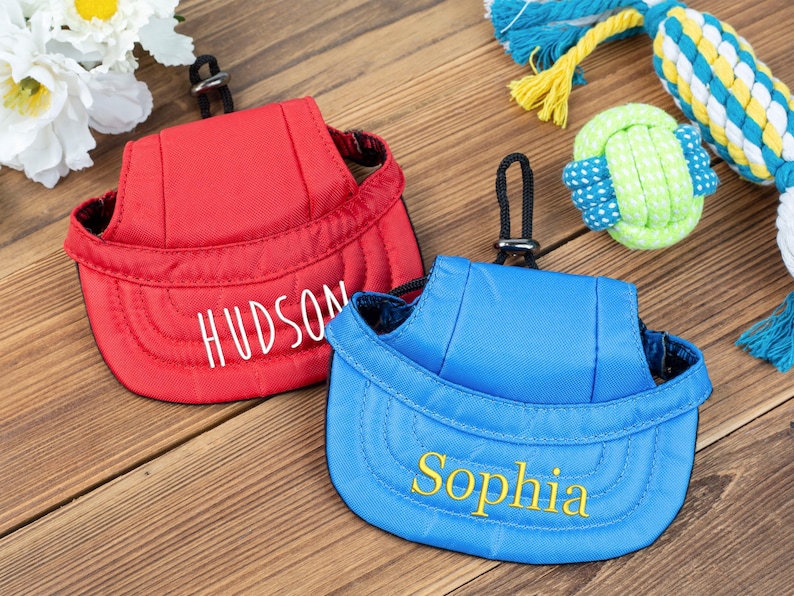 May include: Two personalized dog hats, one red with the name "HUDSON" embroidered in white and one blue with the name "Sophia" embroidered in yellow.