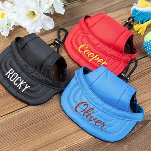May include: Three dog hats with adjustable straps. The hats are black, red, and blue. The hats are embroidered with the names "Rocky", "Cooper", and "Oliver".