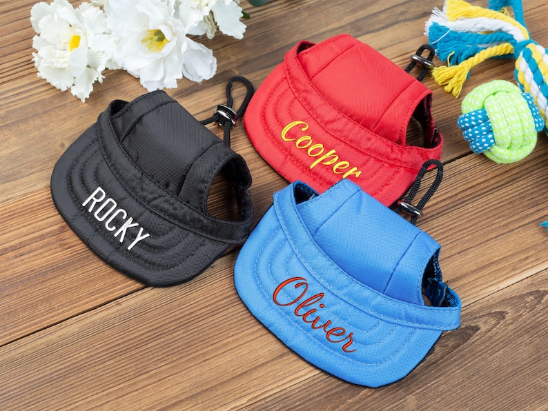 May include: Three dog hats with adjustable straps. The hats are black, red, and blue. The hats are embroidered with the names "Rocky", "Cooper", and "Oliver".