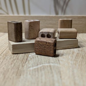 Könnte beinhalten: Eine Sammlung kleiner Bleistiftanspitzer aus Holz in verschiedenen Brauntönen. Einige haben zwei Löcher, andere nur eines. Die Anspitzer sind auf einer hellen Holzoberfläche mit neutralem Hintergrund angeordnet.