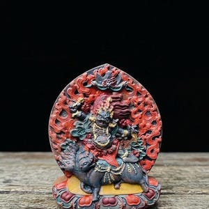 May include: A detailed, multi-colored sculpture of a deity riding a mythical creature. The sculpture features intricate carvings in red, blue, and gold. The deity has a fierce expression and is adorned with ornate jewelry. The background is a stylized, flame-like design.