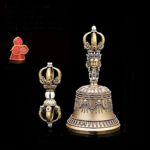 May include: A set of Tibetan Buddhist ritual objects, including a bell and a dorje, in gold and silver tones. The bell features a detailed face and crown design. The dorje has a symmetrical, multi-pronged design. A red and gold object is also visible.