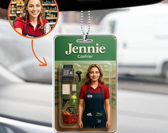 Op de afbeelding: Een auto luchtverfrisser met een lachende vrouw in een rood shirt en blauwe schort, met het label "Jennie Kassierster". Het ontwerp bevat een kassa, scanner en een winkelmandje.
