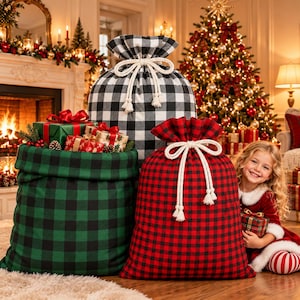 May include: Three large fabric gift sacks featuring a buffalo plaid pattern in black and white, black and green, and black and red. Each sack is cinched at the top with a thick, cream-coloured braided rope drawstring with tasseled ends.