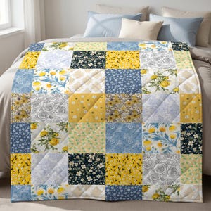 May include: A quilted blanket featuring a patchwork design of various floral patterns in shades of yellow, navy blue, light blue, and white. The squares display motifs of yellow roses, small white blossoms, and intricate line-drawn rose sketches.