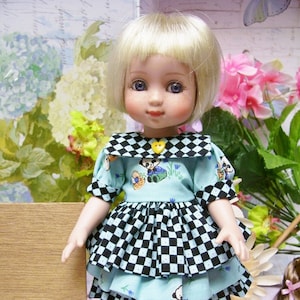 Peut inclure: Une poupée blonde portant une robe à carreaux bleus et noirs avec un col blanc et un imprimé ours panda. La poupée porte des collants blancs et des chaussures noires.