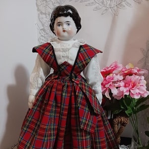 May include: A porcelain doll with black hair and blue eyes wearing a white blouse and a red, yellow, and black plaid skirt.