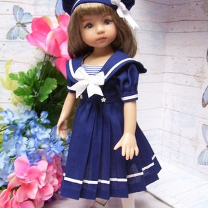 May include: A doll wearing a blue sailor dress with white trim and a white bow. The doll has brown hair and blue eyes and is wearing a blue and white sailor hat.