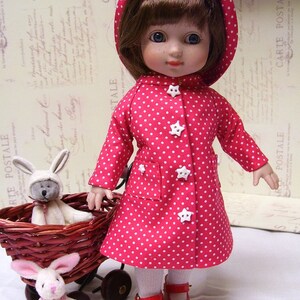 May include: A porcelain doll wearing a red and white polka dot raincoat with a white hood. The doll has brown hair and blue eyes. The doll is wearing red shoes and white socks. The doll is holding a white button in her hand.
