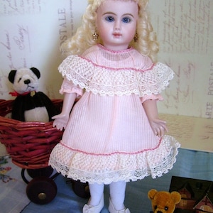 May include: A porcelain doll with blonde hair and blue eyes wearing a pink dress with white lace trim. The doll is holding a teddy bear with brown fur and a blue ribbon. The doll is sitting in a wicker basket with a black and white teddy bear.