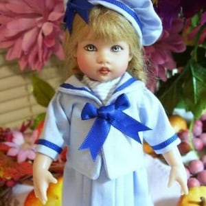 May include: A porcelain doll wearing a blue sailor outfit with a blue bow and a blue and white sailor hat. The doll has blonde hair and blue eyes.