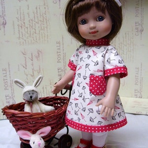 Peut inclure: Une poupée en porcelaine aux cheveux bruns portant une robe blanche à pois rouges et des parapluies noirs imprimés dessus. La poupée tient un panier en osier avec un lapin blanc à l'intérieur. La poupée porte des chaussures rouges avec une boucle dorée.