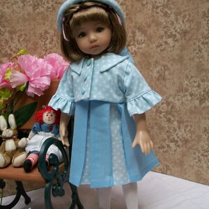 May include: A blue and white polka dot dress with a matching jacket and white hat. The doll is wearing white tights and white shoes. The doll is sitting on a bench with a stuffed animal.